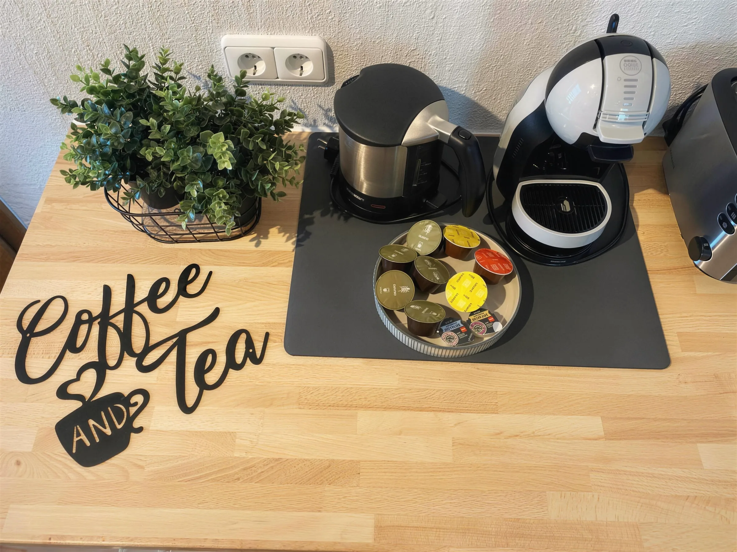 Kaffee-Ecke mit Kaffeemaschine, Wasserkocher und Kaffeekapseln auf Holz